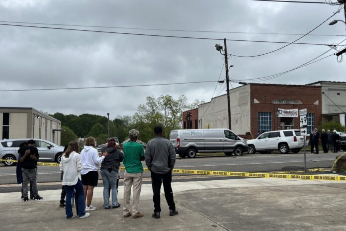 A group of people gather outside the Mahogany’s Masterpiece Dance Studio in Dadeville, Alabama on April 16, 2023. The Alabama Law Enforcement Agency says at least four people were killed in the building on Saturday evening. (Jemma Stephenson/Alabama Reflector)