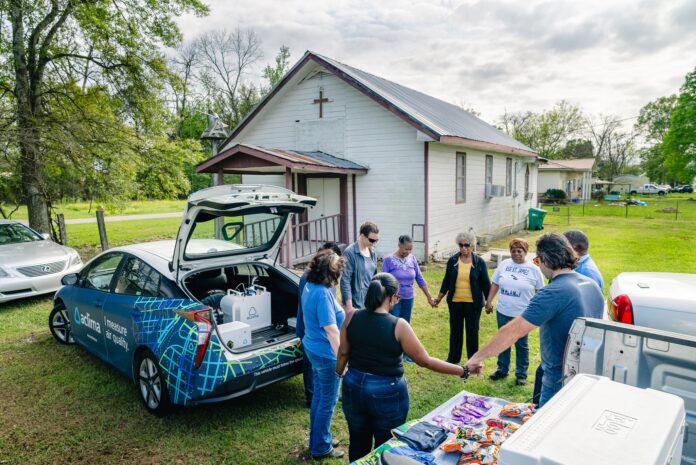 Pastor Harry Joseph leads community members, members of the Louisiana Environmental Action Network and Aclima scientist Aja Ellis in prayer on March 16, 2024 beside the Aclima air-monitoring car in front of the Mount Triumph Baptist Church in St. James Parish. (Zachary Kanzler/LEAN)